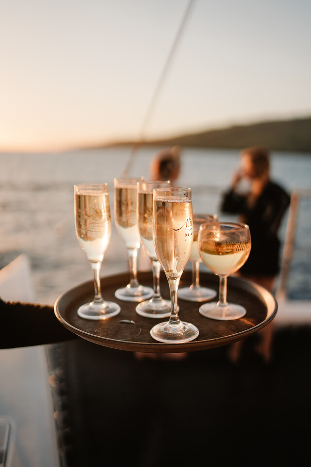 Tray of champagne glasses on a boat at sunset with blurred background.