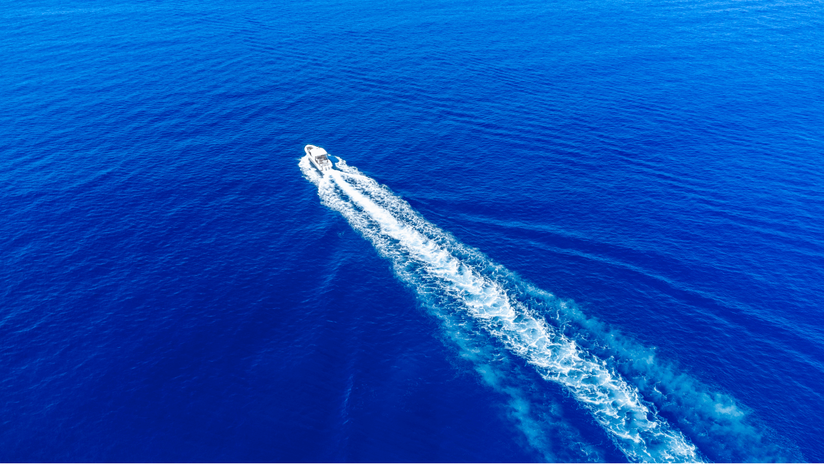 Aerial view of a boat leaving a white wake in the vibrant blue ocean.