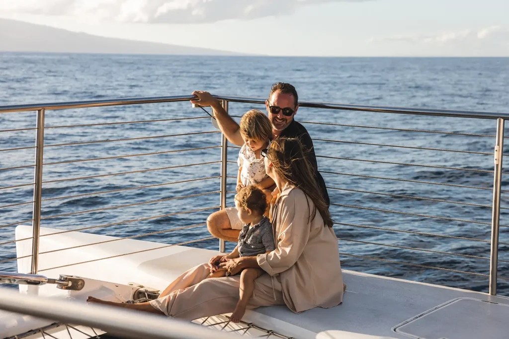 Family relaxing on a boat deck with ocean and mountain in the background.