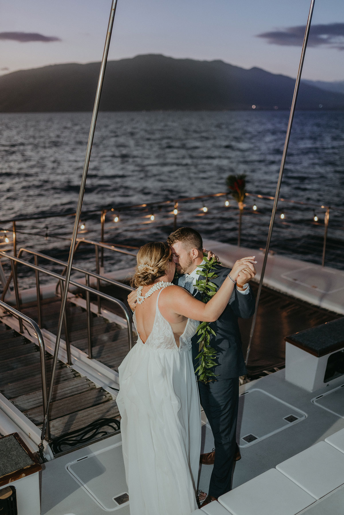 Couple dancing on a yacht at sunset, surrounded by ocean and mountains.