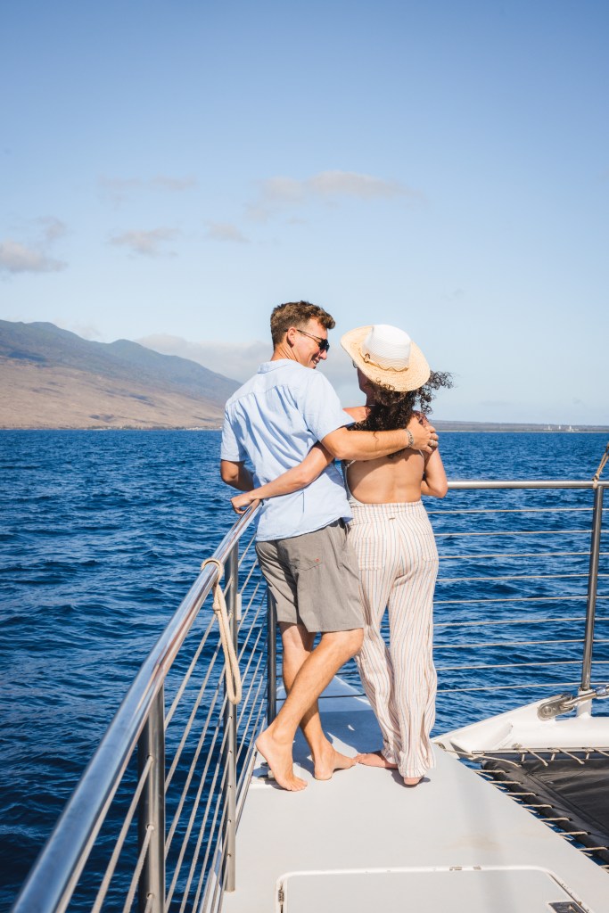 Couple embracing on a boat deck, overlooking ocean and mountains.