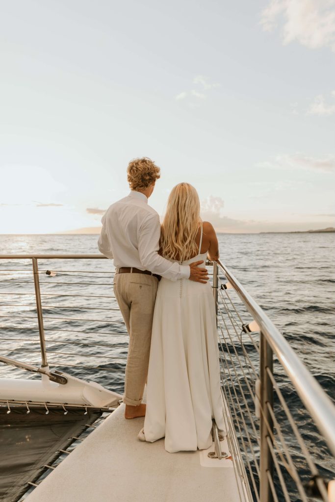Couple embracing on a boat at sunset, looking out over the ocean.