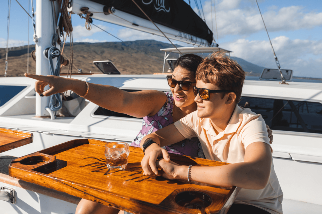Two people on a boat, one pointing, both wearing sunglasses, with sunny skies in the background.