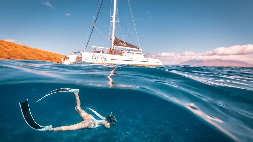 Underwater view of snorkeler near sailboat with clear sky above.