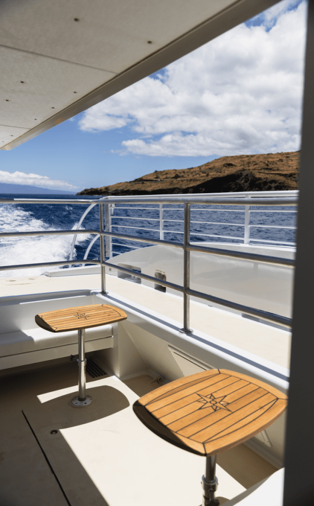 Boat deck with two wooden stools and ocean view, blue sky, and distant hills.