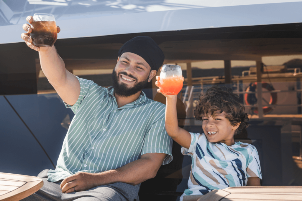 Smiling man and boy toasting with drinks on a boat.