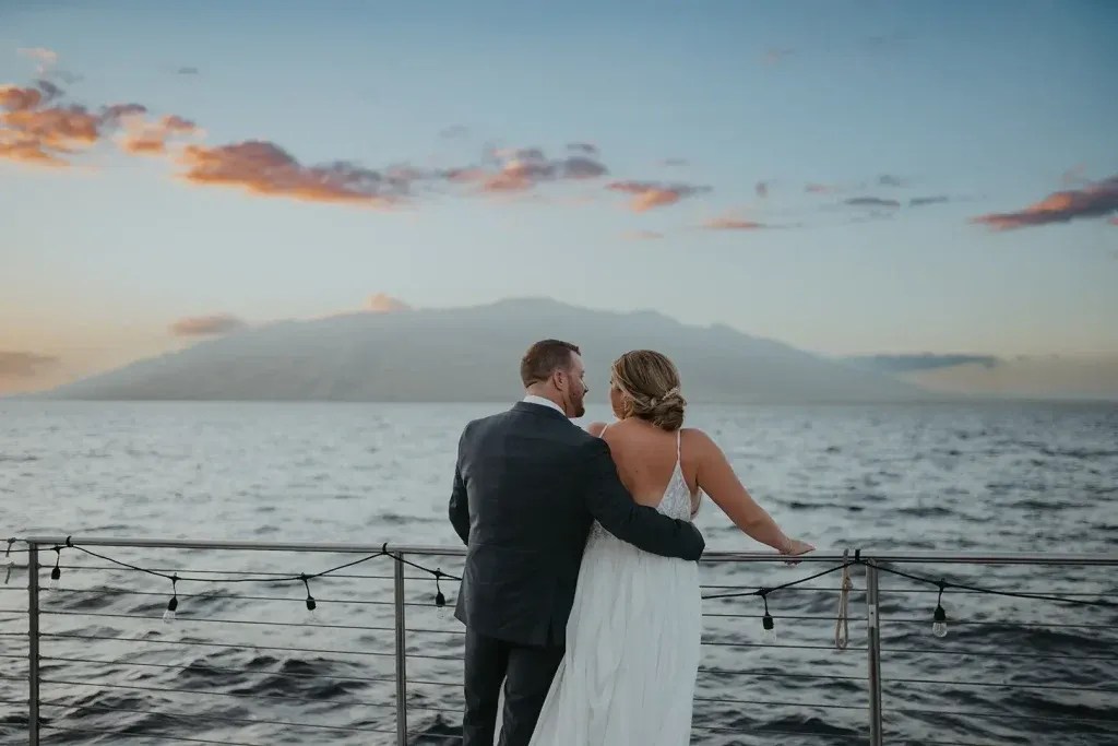 Couple embracing on a boat, watching ocean sunset with distant mountains.