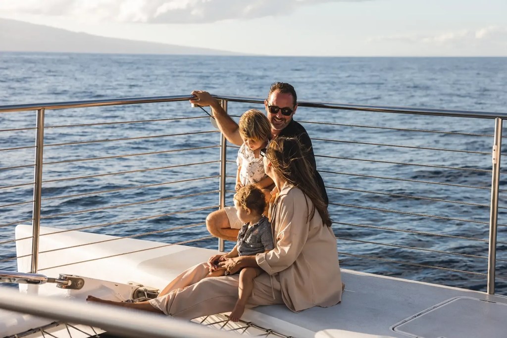 Family relaxing on a boat deck with ocean and mountain in background.