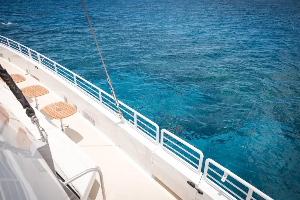 Yacht deck with chairs overlooking clear blue ocean water.