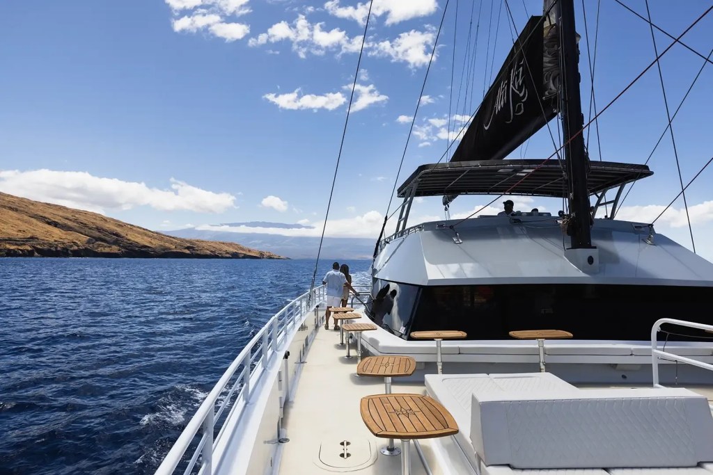 View from a yacht sailing near an island with blue skies and scattered clouds.