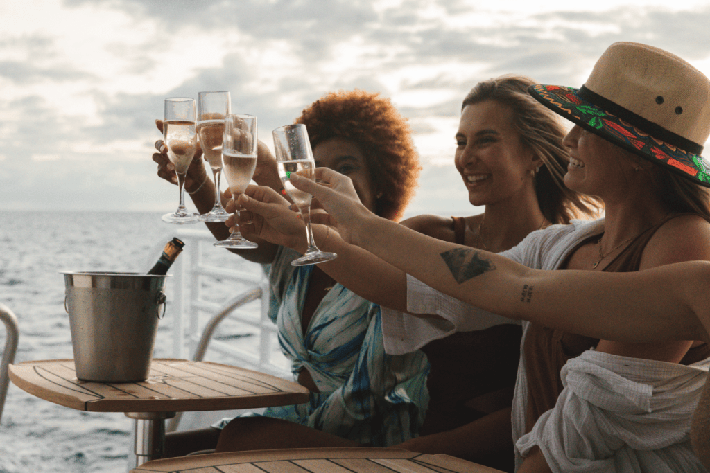 Four people toasting with champagne glasses on a boat during sunset.