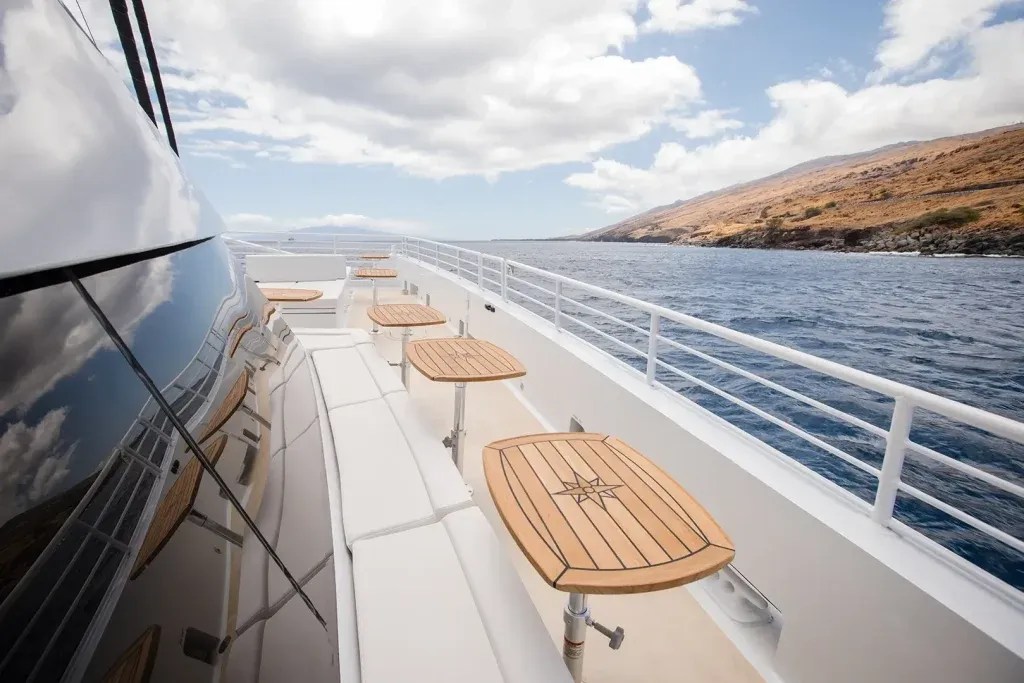 Yacht deck with wooden tables, ocean and island view under a cloudy sky