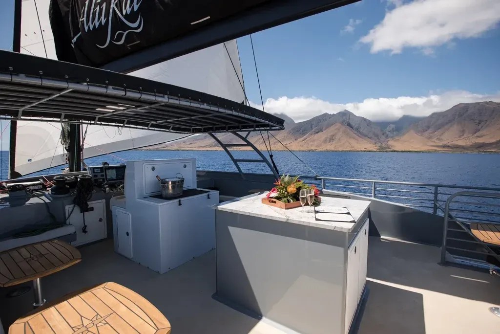 Sailing yacht deck with seating and mountain view across calm water under blue sky.