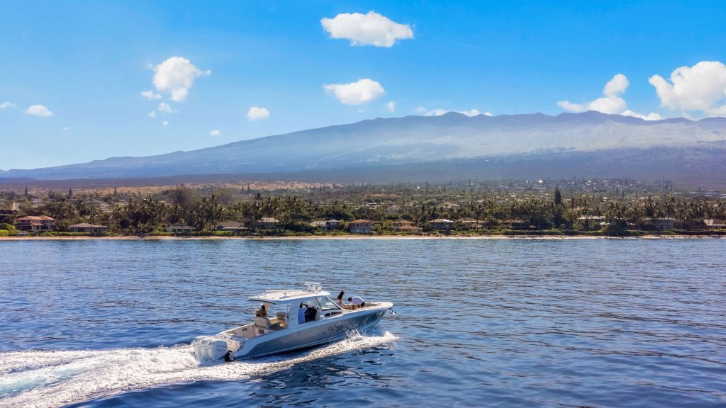 Boat cruising on water with mountain and clear blue sky in the background.