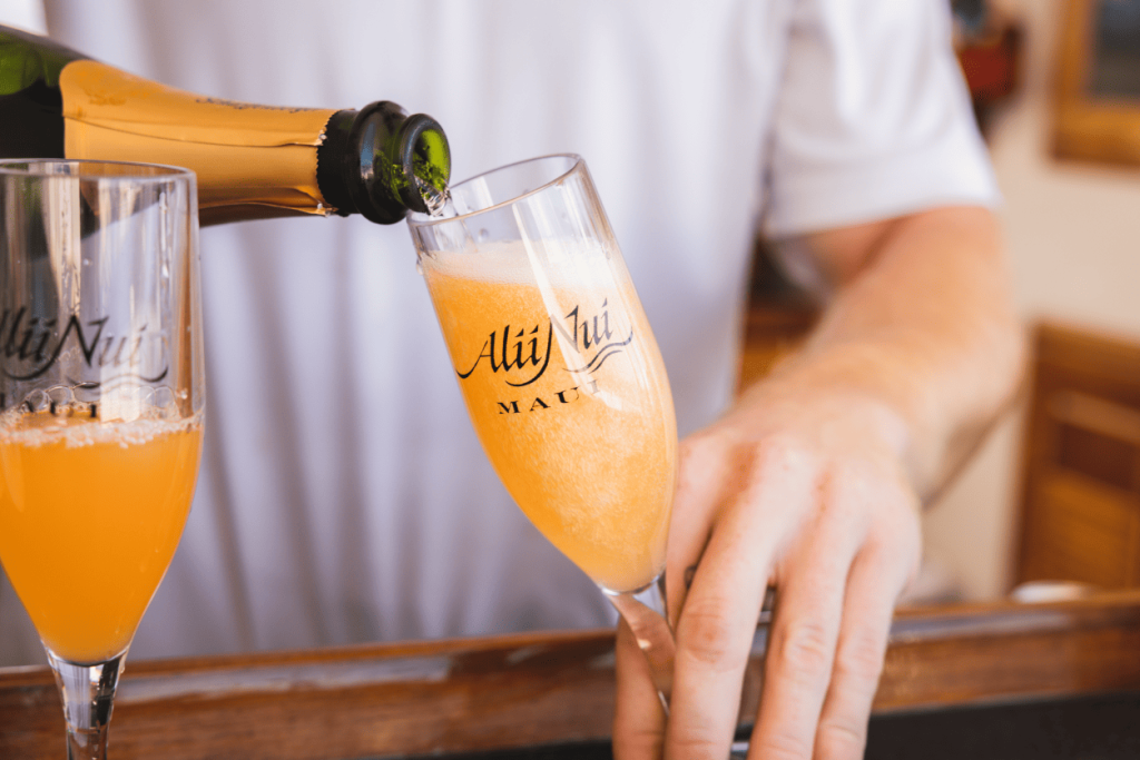 Person pours champagne into flute with orange drink at a bar.