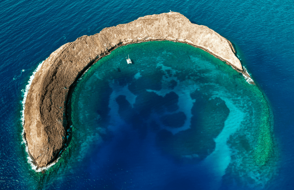 Aerial view of a crescent-shaped island with clear blue waters surrounding it.