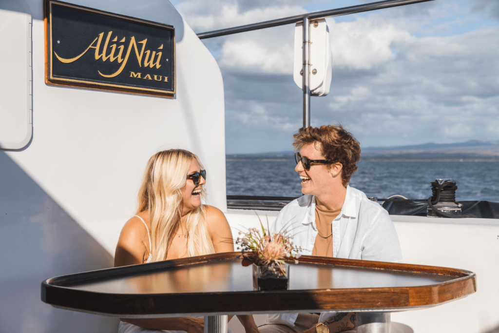 Two people smiling at each other on a boat with ocean in the background.