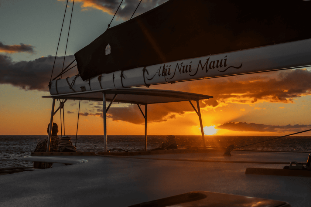 Sailboat at sunset with a dramatic orange sky and dark clouds.