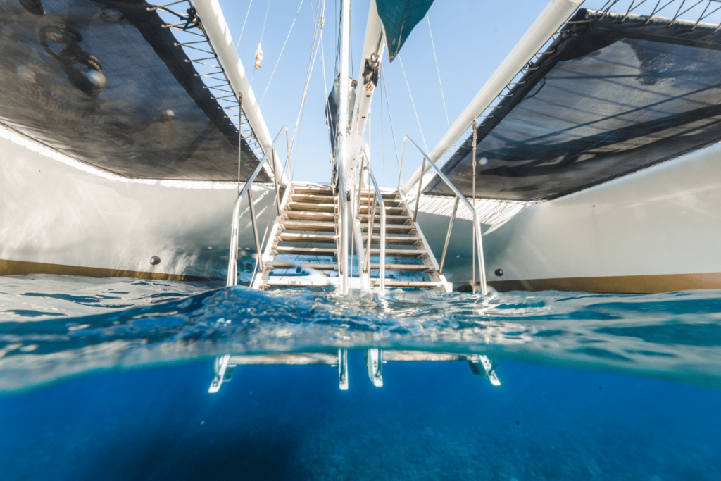 Underwater view of a catamaran's ladder descending into the clear blue ocean.