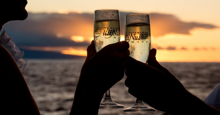 Two people clinking glasses of sparkling wine at sunset by the ocean.