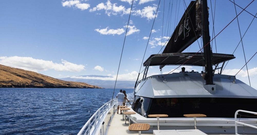 Sailing yacht on calm ocean with clear sky and distant land on the left.