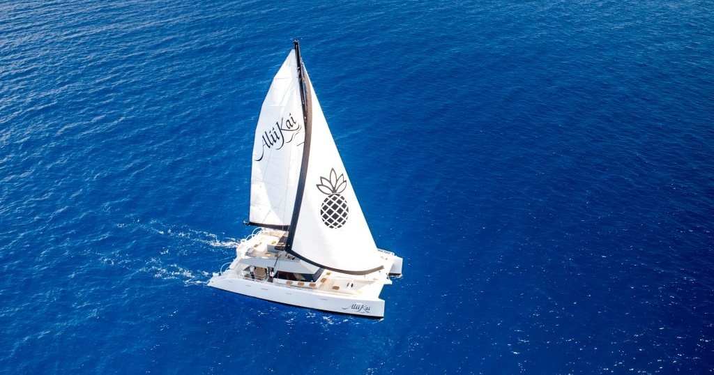 Aerial view of a sailboat with logo sailing on clear blue ocean waters.