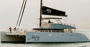 A sleek, modern catamaran sailboat on calm waters with the name Alii Kai on its side.
