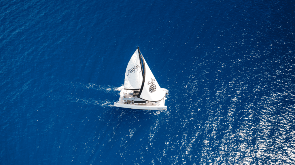 Aerial view of a sailboat with white sails on a deep blue sea.