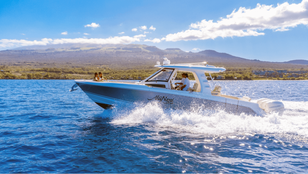 Motorboat cruising on blue water with mountains and blue sky in the background.