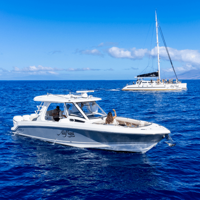 Two boats on a calm ocean under clear blue skies, a motorboat in the foreground and a sailboat in the background.